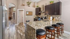 A modern kitchen with granite countertops, dark cabinets, and a central island with bar stools.