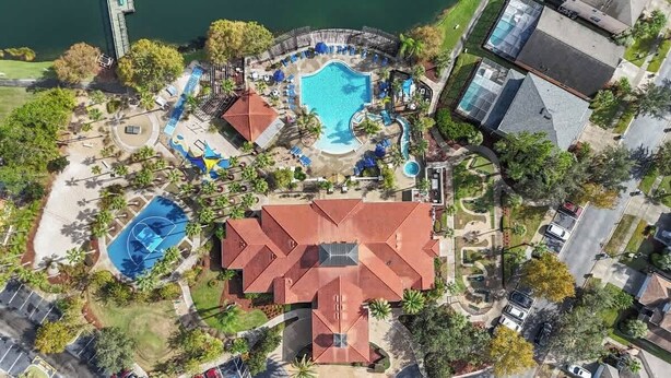 An aerial view of a resort with a large swimming pool, a tennis court, and a central building with a red roof.