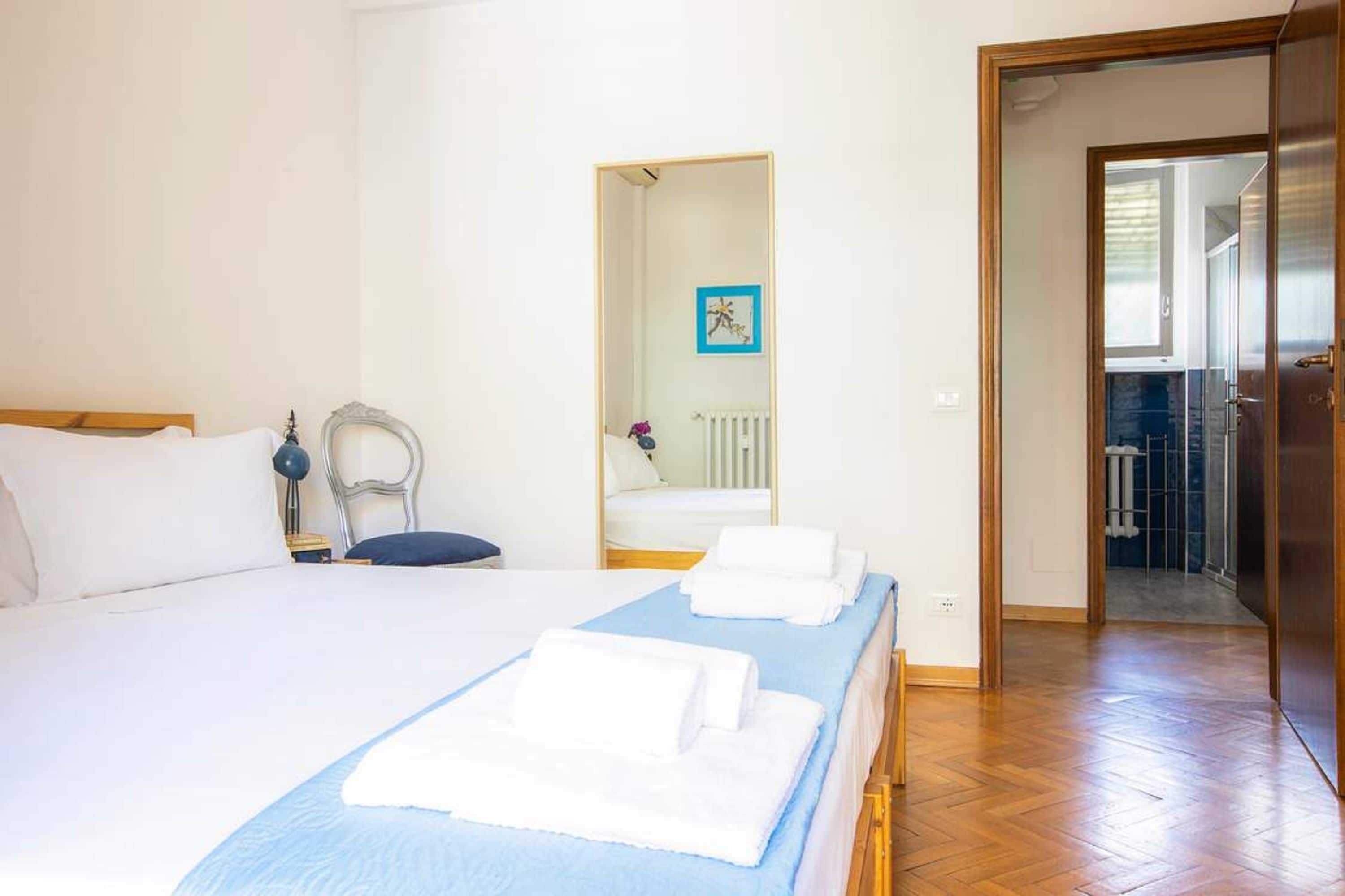 Ett hotellrum med en stor säng, ett sängbord, en stol, en spegel och ett badrum som syns genom en öppen dörr.