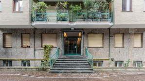 A building with a stone facade, a green entrance, and a balcony with plants. - Casa Giulia in Milano (Milan)