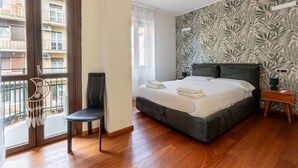 A bedroom with a bed, a chair, a bedside table, a window with a view of buildings, and a wall with a leaf pattern. - Casa Giulia in Milano (Milan)