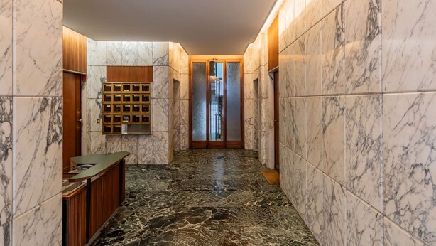 A marble-floored hallway with a reception desk, wooden paneling, and a glass door leading to another room. - Casa Giulia in Milano (Milan)