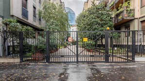 A gated entrance to a residential building with a clear view of a modern glass building in the background. - Casa Giulia in Milano (Milan)