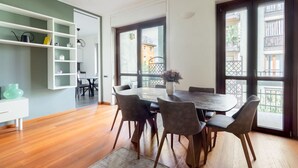 A dining area with a round table, six chairs, and a vase of flowers. There is a white shelving unit with various items on the left. - Casa Giulia in Milano (Milan)