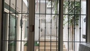 Una vista attraverso un cancello in metallo su un cortile con gradini che conducono a una porta, immerso nel verde e con una lavatrice visibile a destra.
