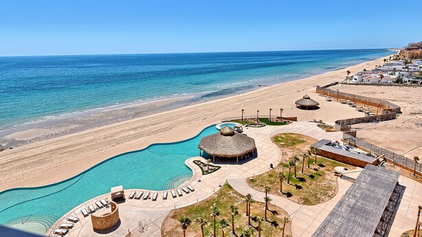 Un resort con piscina, playa y edificaciones de techo de paja.