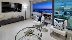 Una sala de estar moderna con un televisor grande, un sofá, una mesa de centro y un balcón con vistas.