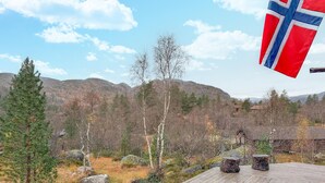 A wooden deck with a flag, surrounded by trees and mountains. - 3 bedroom cozy home in Tjørhom (Tjørhom)