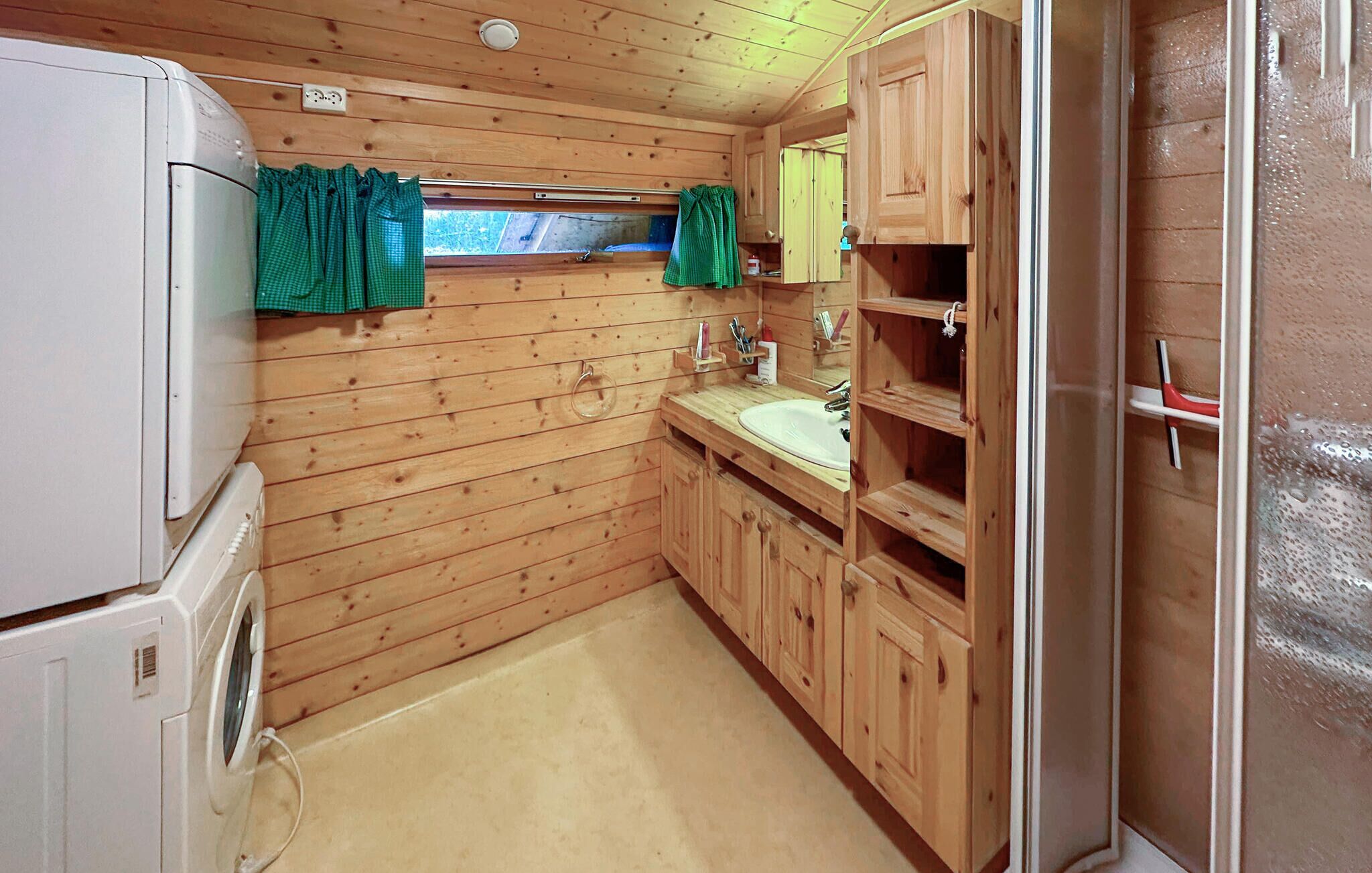 A compact wooden cabin-style bathroom with a sink, mirror, and a window with curtains.