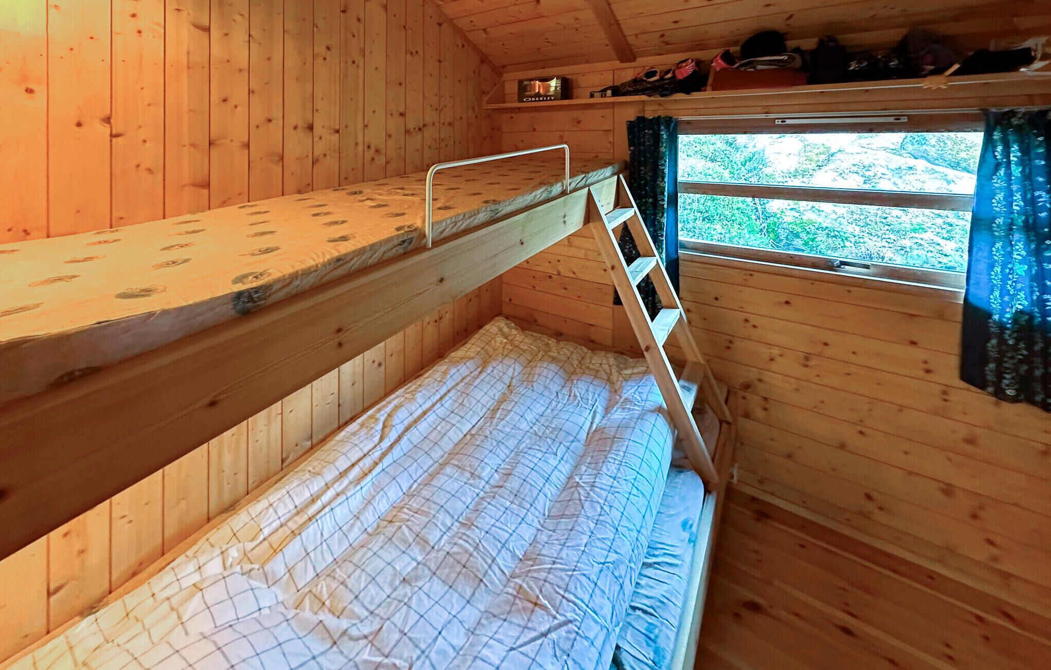Une chambre avec un lit superposé, des murs en bois et une fenêtre avec des rideaux.