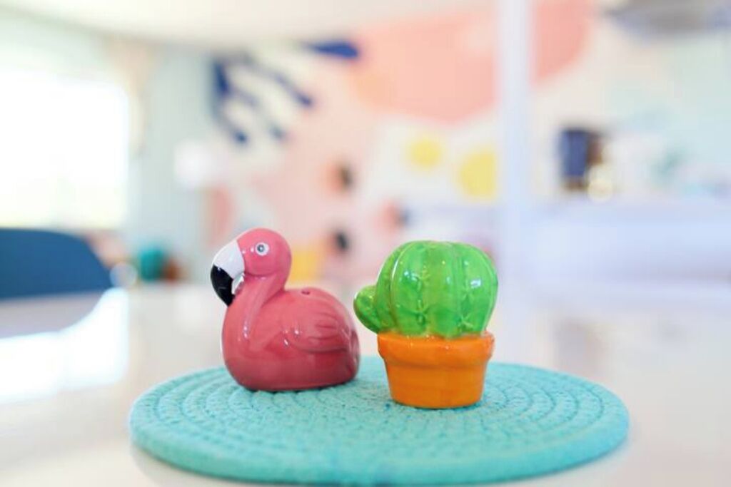 Een klein, kleurrijk cactusplantje en een roze flamingo-beeldje op een turquoise onderzetter.