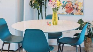 A dining area with a round table, teal chairs, a floral painting, and a ceiling light fixture. - Casa De Colores w/ Arcade, hot tub + more - J Tree

 (Joshua Tree)