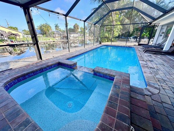 Une piscine dotée d’une enceinte en verre, entourée d’une terrasse offrant une vue sur des palmiers et un bâtiment en arrière-plan.