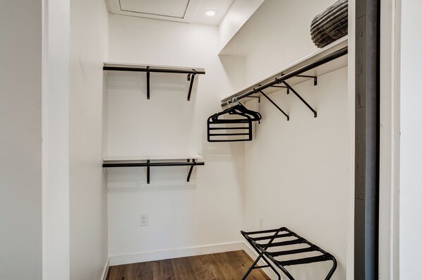 A narrow hallway with white walls and wooden flooring. There are three black metal racks mounted on the walls, one with a basket and two with shelves.