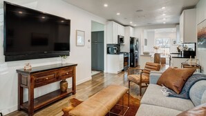 A modern living room with a large flat-screen TV, wooden console table, and a comfortable seating area with a sofa and chairs.