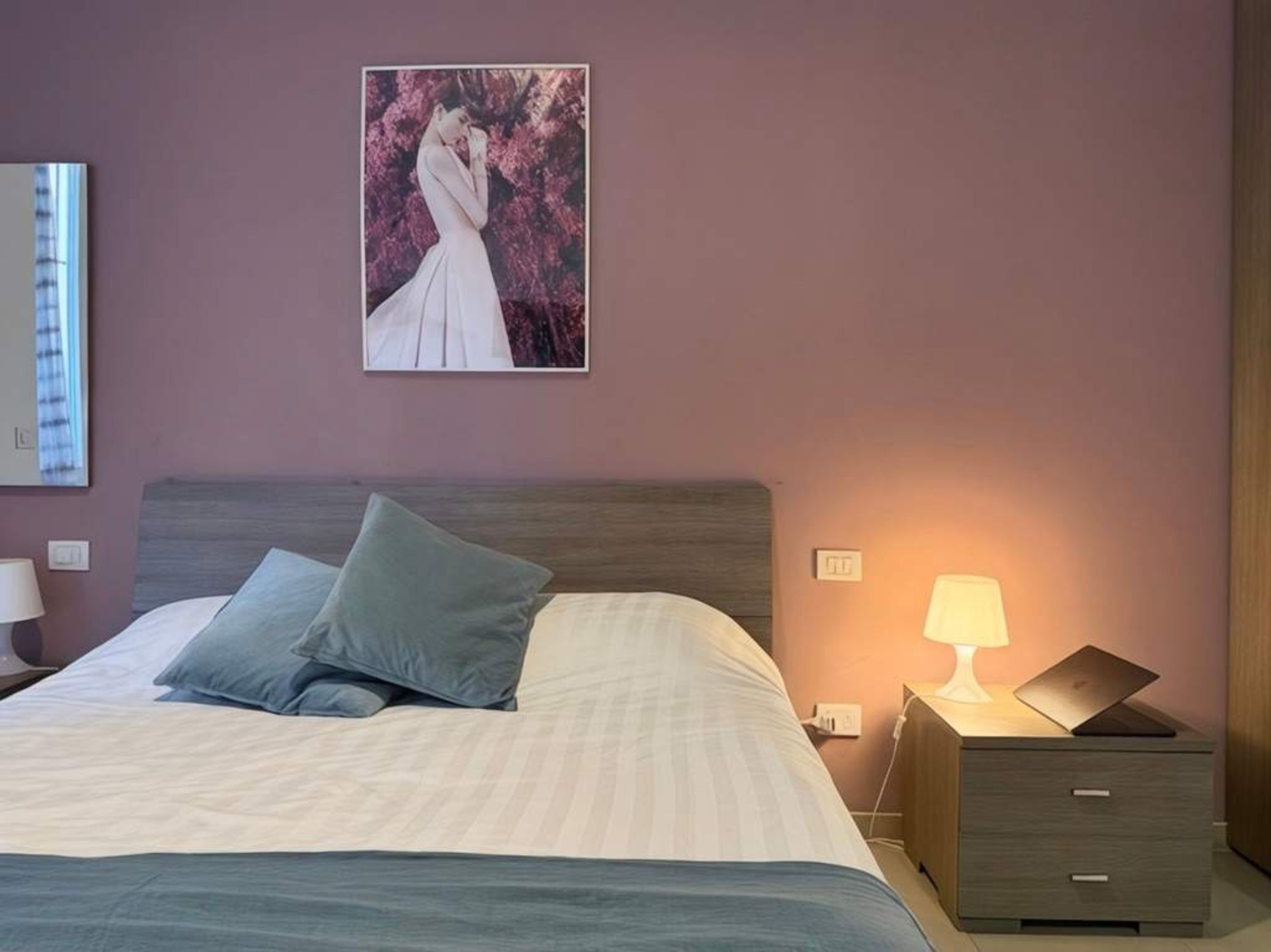 Une chambre à coucher avec un lit, des oreillers, une table de chevet avec une lampe et un tableau au mur.