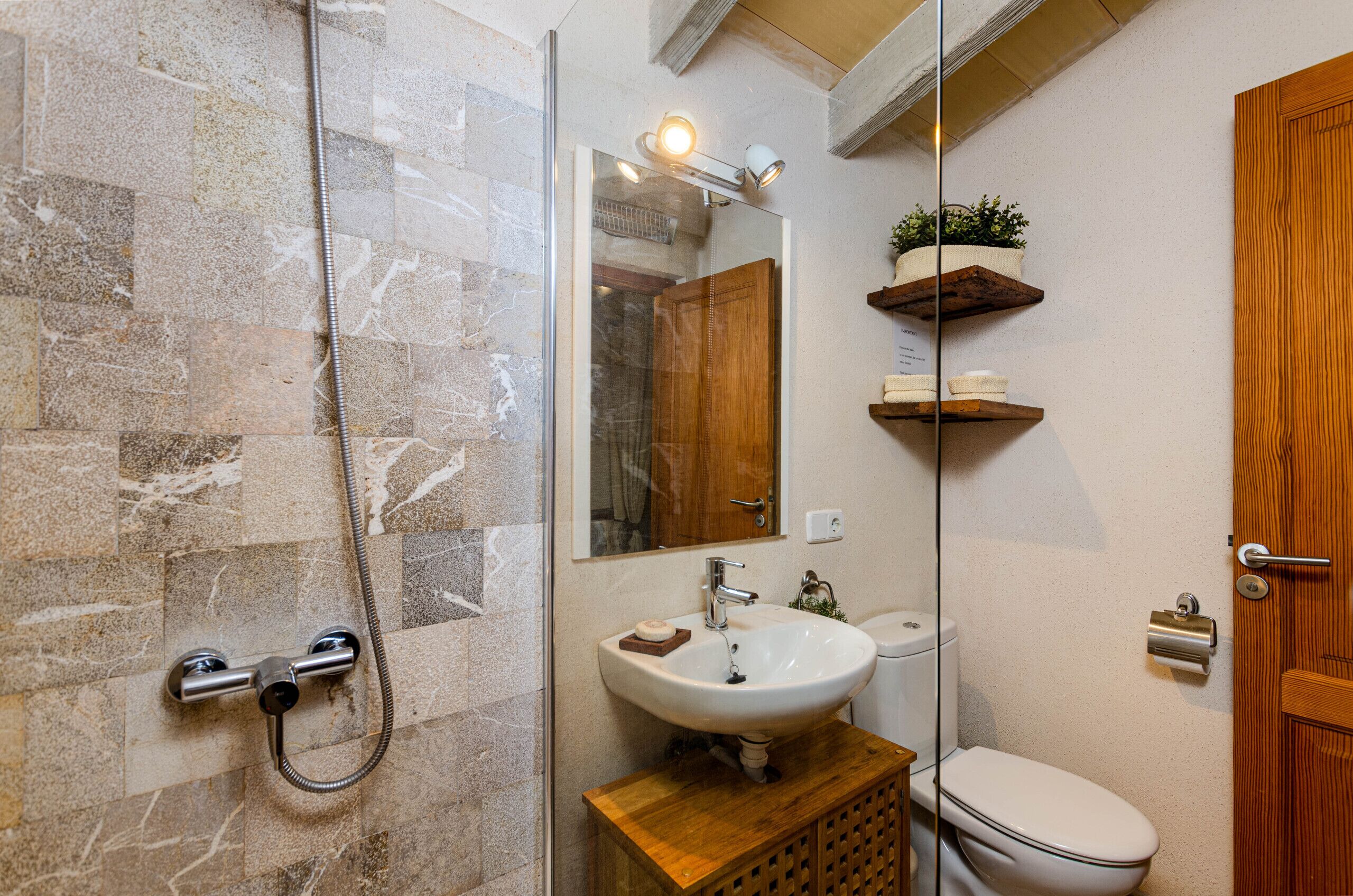 Een badkamer met een douchecabine van glas, een houten wastafelmeubel, een witte wasbak en een toilet.