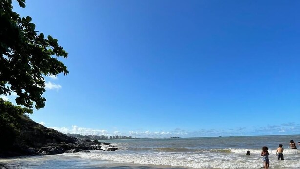 Une plage avec une eau calme, un ciel dégagé et quelques personnes profitant du bord de mer.