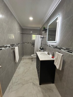 Bathroom features a large mirror, black countertop, and white sink, along with a shower area and towel storage.