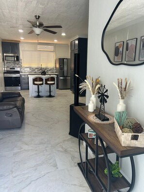 Relax in a stylish living area with a comfortable sofa, coffee table, and TV stand, connected to a kitchen with a central island and bar stools.