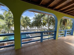 Ein überdachter Außenbereich mit Pool, Fliesenboden und Blick auf Palmen und einen Strand.