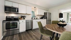 Una cocina moderna con electrodomésticos de acero inoxidable, armarios blancos y un comedor con una mesa de madera y sillas verdes.