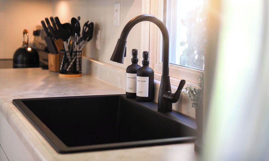 A kitchen sink with a modern faucet, a window with a view, and two bottles of dish soap on the counter.