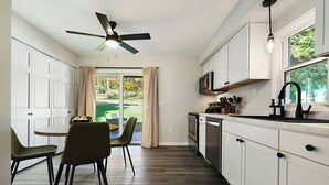 Una cocina moderna con armarios blancos, ventilador de techo y comedor con dos sillas.