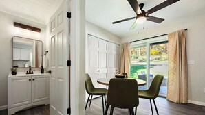 Una cocina moderna con armarios blancos, una zona de comedor con sillas verdes y un ventilador de techo.