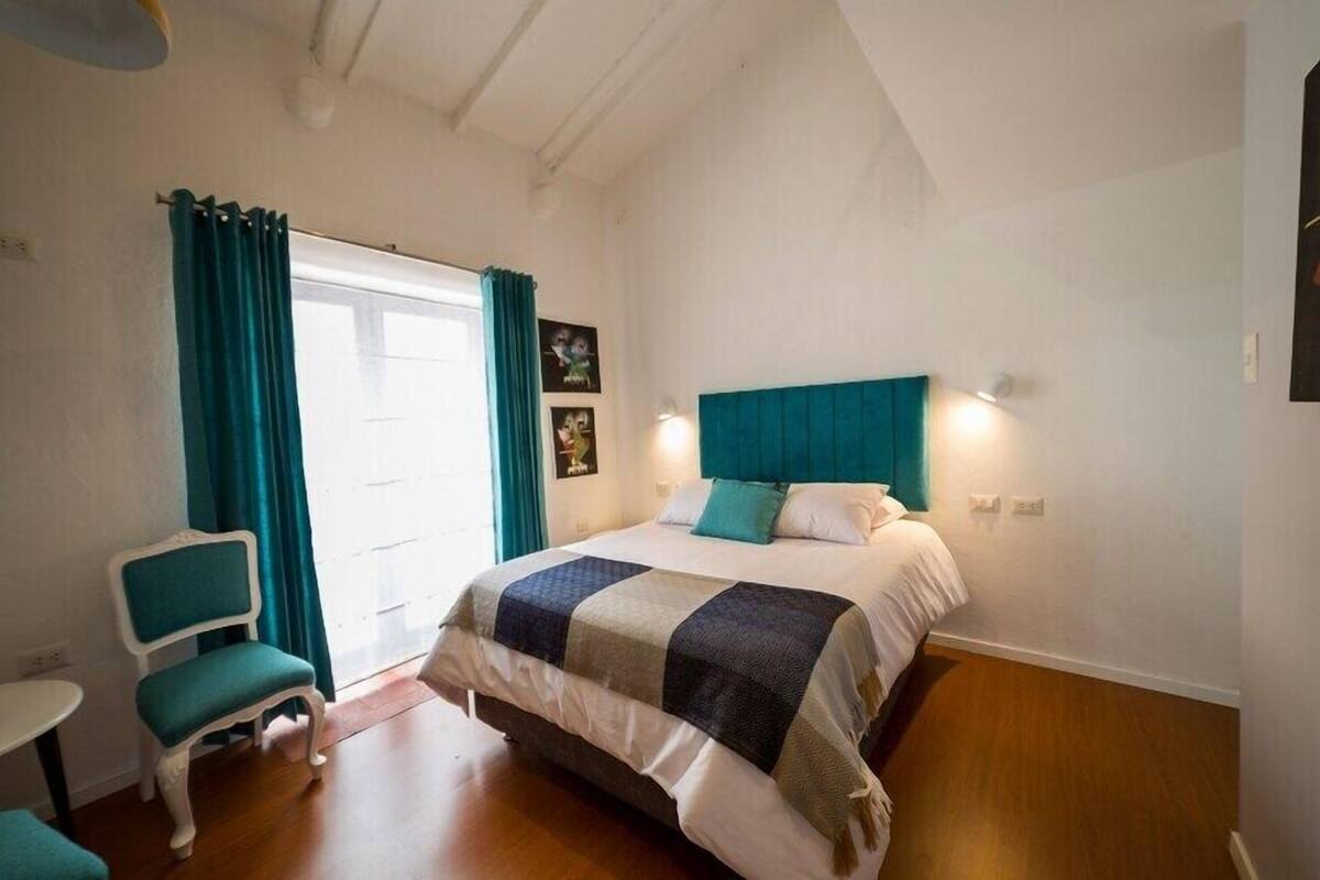 A bedroom with a bed, a chair, a table, and a window with curtains.