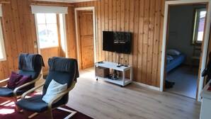 A cozy room with wooden walls, a TV on a stand, a bed, and two chairs with cushions. - 4 Star Holiday Home in Syssleback (Sysslebäck)