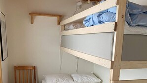 A bunk bed with white and blue bedding, a wooden chair, and a white wall with a picture frame.