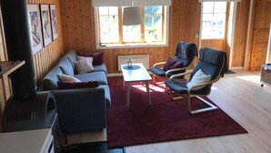 A cozy room with a wooden interior, a sofa, two armchairs, a small table, and a large window with a view of greenery. - 4 Star Holiday Home in Syssleback (Sysslebäck)