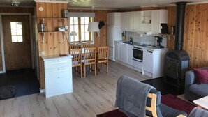 A compact kitchen with white cabinets, a stove, and a wood-burning stove. There is a dining area with wooden chairs and a table. - 4 Star Holiday Home in Syssleback (Sysslebäck)