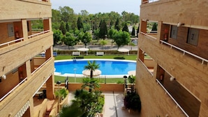 Un edificio de varios pisos con piscina, rodeado de vegetación y mobiliario exterior.