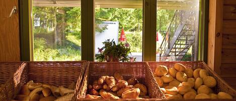A display of bread and pastries in wicker baskets by a window with a view of greenery and a building outside.
