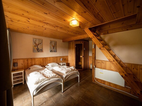 A cozy bedroom with two beds, wooden ceiling beams, and a radiator. - Escape in Dochamps Chalet (Manhay)