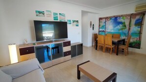 Ein Wohnzimmer mit Fernseher, einer Couch, einem Couchtisch und einem Essbereich mit Stühlen und Tisch.