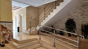 Una escalera moderna con barandillas metálicas, suelo de mármol y pared de ladrillo.