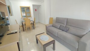 Una sala de estar con sofá, una mesa de centro, televisor y una mesa de comedor con sillas.