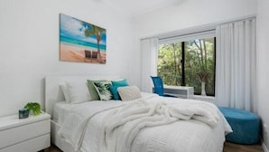A bedroom with a bed, a nightstand, a window with curtains, and a painting of a beach scene. - Currumbin Escape 2 BDR Water Views (Currumbin)