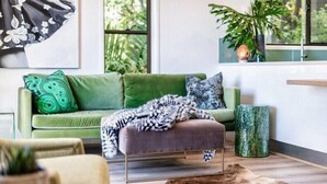 A green sofa with patterned cushions, a wooden bench, a green vase, and a plant in a modern living room with large windows. - Currumbin Escape 2 BDR Water Views (Currumbin)