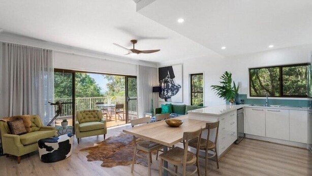 A spacious living area with a dining table, green armchairs, and a large window overlooking greenery. - Currumbin Escape 2 BDR Water Views (Currumbin)