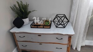 A white dresser with three drawers, a black geometric object, a 'Hello!' sign, a remote control, and a potted plant. - Charming Cozy Cottage Pittsboro  (Pittsboro)