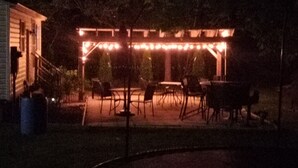 An outdoor patio area with a pergola covered in string lights, surrounded by chairs and tables. - Charming Cozy Cottage Pittsboro  (Pittsboro)