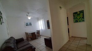 A living room with a dark brown sofa, a dining table with chairs, a ceiling fan, and a painting on the wall. - Round Trip - LA06-Bertioga, SESC, Riviera, Vista Linda, Indaiá (Jardim Rafael Bertioga)