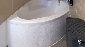 Een badkamer met een vrijstaand bad, een douchekop en een klein plankje met toiletartikelen.