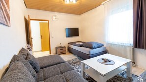 Een moderne woonkamer met een bank, salontafel, televisie en een raam met gordijnen.