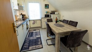 Een compacte keuken met een eethoek, een magnetron, een waterkoker en een kleine koelkast.
