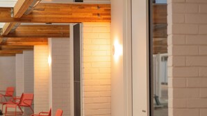 A corridor with white brick walls, wooden beams, and red chairs. - Kar-Rama Hotel  (Mildura)